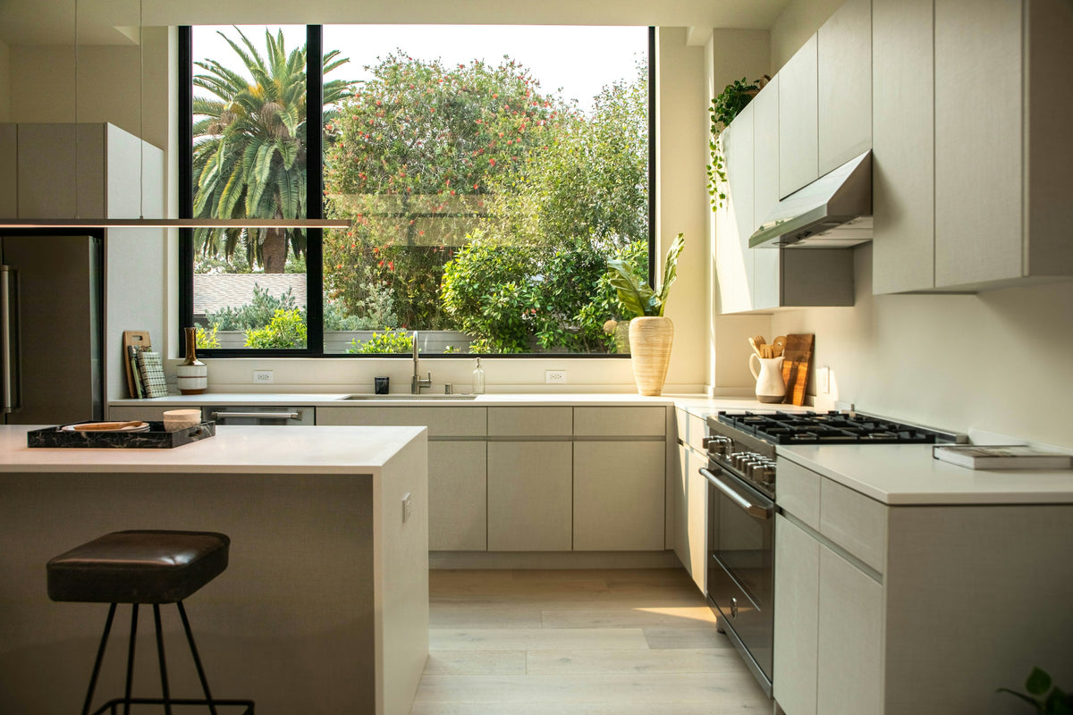 A sunlit kitchen with warm wood, white cabinetry and a garden view. Category inspiration only.